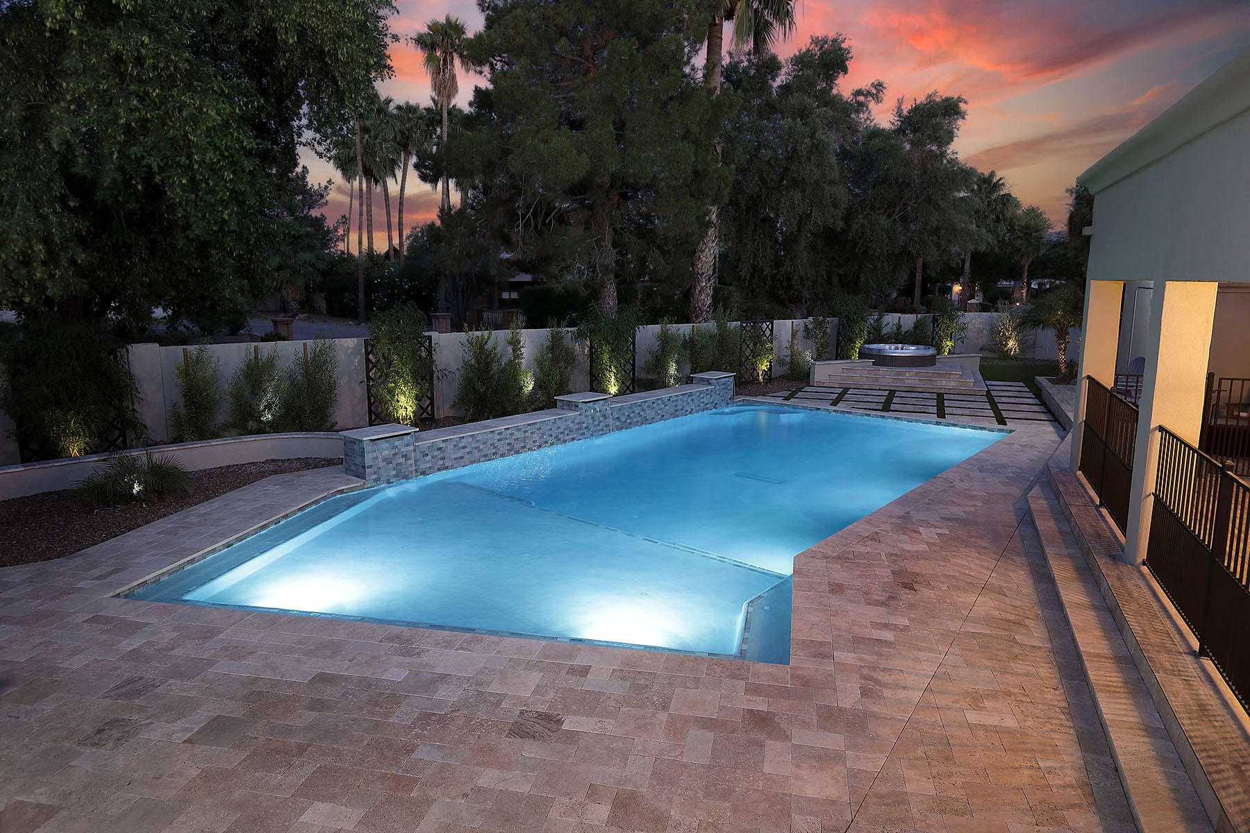 Luxury custom swimming pool with spa and travertine deck lit at dusk in an Arizona backyard built by Optima Pools