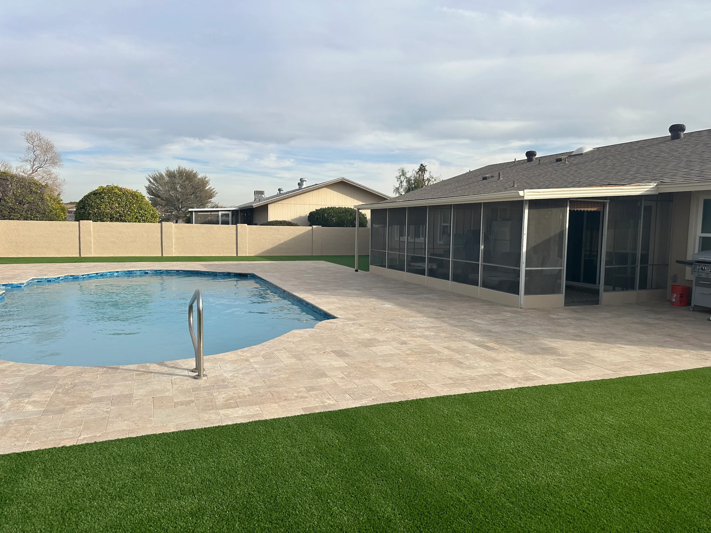 Completed pool remodel with new travertine decking and artificial turf lawn from a happy Optima Pools customer in Surprise, AZ